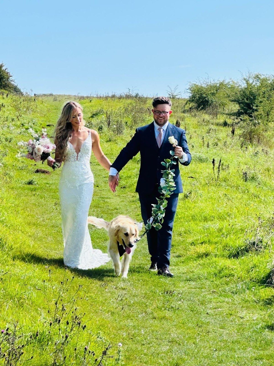 A bride and groom walking hand in hand with a golden retriever leading the way